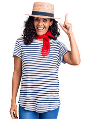 Wall Mural - Middle age beautiful woman wearing casual striped t shirt and summer hat pointing finger up with successful idea. exited and happy. number one.