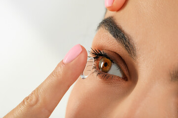 Poster - Young woman putting contact lens in her eye, closeup