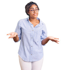 Sticker - Young african american woman with braids wearing casual clothes and glasses clueless and confused expression with arms and hands raised. doubt concept.