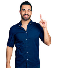 Sticker - Young hispanic man with beard wearing casual blue shirt pointing finger up with successful idea. exited and happy. number one.