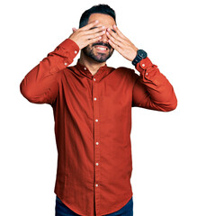 Poster - Young hispanic man with beard wearing casual shirt covering eyes with hands smiling cheerful and funny. blind concept.