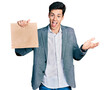 © Krakenimages.com - Young hispanic business man holding paper bag with bread celebrating achievement with happy smile and winner expression with raised hand