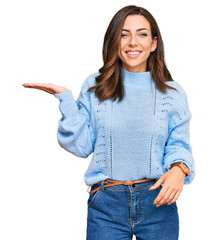 Wall Mural - Young brunette woman wearing casual winter sweater smiling cheerful presenting and pointing with palm of hand looking at the camera.