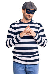 Poster - Young handsome man wearing burglar mask hands together and fingers crossed smiling relaxed and cheerful. success and optimistic