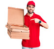 © Krakenimages.com - Young handsome man with beard wearing delivery uniform holding boxes with pizza smiling happy pointing with hand and finger