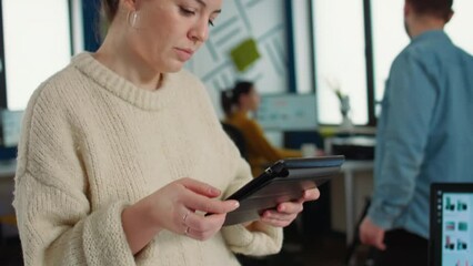 Wall Mural - Portrait of woman in startup office picking up tablet with business charts and interacting with touchscreen to work on financial data. Employee holding digital device to analayze market share.