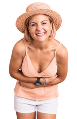 Poster - Young blonde woman wearing summer hat smiling and laughing hard out loud because funny crazy joke with hands on body.