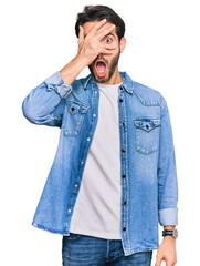 Sticker - Young hispanic man wearing casual clothes peeking in shock covering face and eyes with hand, looking through fingers with embarrassed expression.