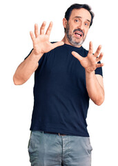 Poster - Middle age handsome man wearing casual t-shirt afraid and terrified with fear expression stop gesture with hands, shouting in shock. panic concept.