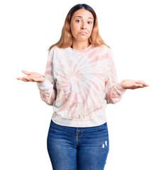 Sticker - Beautiful young woman wearing casual tie dye sweatshirt clueless and confused expression with arms and hands raised. doubt concept.