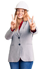 Poster - Beautiful young woman wearing architect hardhat smiling looking to the camera showing fingers doing victory sign. number two.