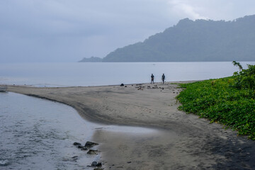 Two Melanesian people walking and strolling along a black sandy beach with ocean views on tropical island of Bougainville, Papua New Guinea