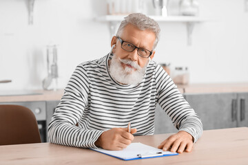 Wall Mural - Male psychologist with earphones and clipboard video chatting in kitchen