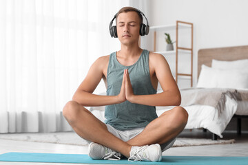 Poster - Young man with headphones meditating on mat in bedroom