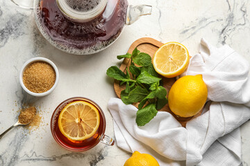 Glass cup of black tea with lemon, cane sugar, mint and teapot on light background