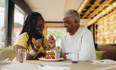 Wall Mural - Happy senior couple sharing a delicious cake in a cafe