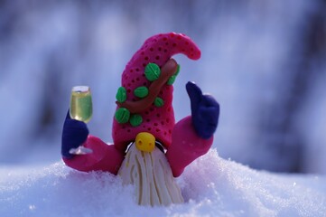 Wall Mural - A fabulous dwarf made of plasticine with a glass of champagne in his hand against the background of snow. Beautiful fabulous Christmas figurines.