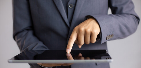 Poster - Close up businessman finger touching and pointing on black blank screen tablet grey background.
