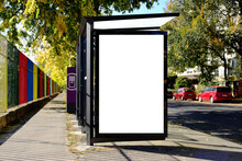 Glass Bus Shelter At Busstop. Blank White Lightbox Sign. Aluminum Structure. Urban Setting. City Street Background. Asphalt Road. Empty Poster Ad Commercial Space With Urban Background For Mockup