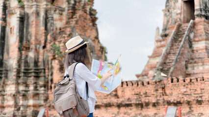 Wall Mural - Hipster woman traveler with backpack holding map and exploring on temple, travel concept, space for text. wanderlust