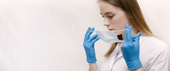 Wide banner. A blonde doctor wearing a medical mask puts on medical gloves confidently and professionally. Female doctor in a medical mask and gloves. Doctor or scientist concept.