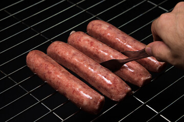 Wall Mural - Raw sausages on a grill grate on a black background. Meat products at home. Tongs take sausage on the grill