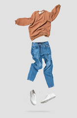 Wall Mural - Fashionable flying brown cotton stylish sweatshirt, blue jeans, leather sneakers isolated on gray background. Clothes, shoes, fashion, clean jacket pullover, creative mockup for design