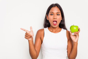 Poster - Young Indian woman holding an apple isolated on white background pointing to the side