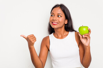 Wall Mural - Young Indian woman holding an apple isolated on white background points with thumb finger away, laughing and carefree.