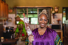 Retrato De Una Hermosa Mujer Afrocaribeña Muy Sonriente Con Un Vestido Caribeño De Pie En El Interior De Su Casa Sosteniendo Con Su Mano Un Rodillo De Madera. 