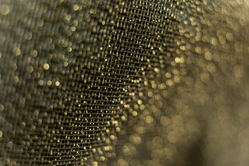 Background image of gold sparkly mesh ribbon on metallic fabric in selective focus. Macro with extremely shallow dof.