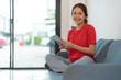 © Naypong Studio - A beautiful woman in a red shirt sitting on the sofa with a tablet.