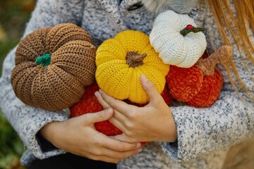  Cute child girl holding handmade knitted pumpkins in her hands on the background of the autumn forest. Concept of cozy autumn and home decor