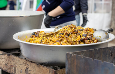 street food national holiday city day.rice with pork chicken meat vegetables in large saucepans.people in background cook man woman,smoke coal fire.mix spicy seafood mussels shrimps squid in cauldron.