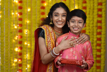 Wall Mural - Young woman and son celebrating diwali,holding plate of diyas, gift boxes 