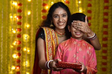 Wall Mural - Young woman and son celebrating diwali,holding plate of diyas, gift boxes 