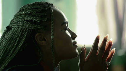 Wall Mural - Faithful African American young woman praying to God. Hopeful South american latina Brazilian adult girl in prayer at home