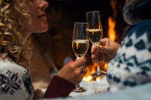 Close Up Of Couple In Love Clinking With Champagne Flutes During Christmas Holiday Celebration. Fireplace In Background. Winter Holidays Eve With Romantic Man And Woman Drinking Celebrating Together