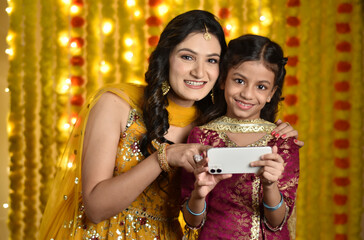 Wall Mural - Happy young woman and daughter celebrating diwali and taking selfie