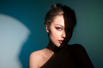 Creative close-up portrait of a beautiful girl with eyeliner standing on stage with a beam of bright light