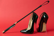 Black shiny high heel shoes and a whip on a red background