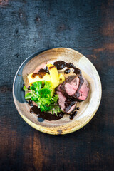 Wall Mural - Traditional German venison roast with boiled potato, basil pesto and spicy red wine sauce served as top view on a Nordic design plate