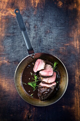 Traditional German venison roast with juniper berry and rosemary in spicy red wine sauce served as top view in a frying pan