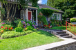 © Dolores  Harvey - The front yard of a dark blue house with a vibrant red door. The building has a glass window with white trim. The colorful garden has green grass, red, pink, and yellow flowers, shrubs, and trees.