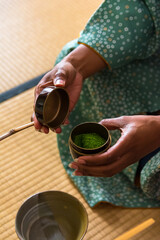 African American woman guest hands holding chashaku bamboo matcha tea spoon and opens Natsume lacquered wooden matcha tea container during a Japanese traditional tea ceremony