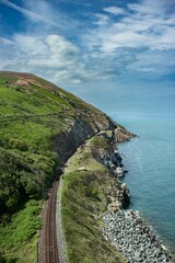 Sticker - Vertical shot of the rocky green cliffs with a trail near water near Bray and Greystones in Ireland