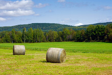 A Picture Of A Field With Haystack, Hay Bales With Mountains