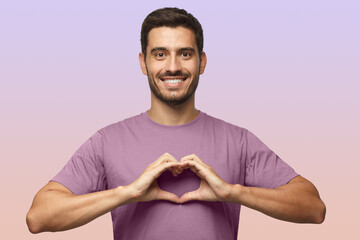 Wall Mural - Portrait of smiling man in t-shirt showing heart sign isolated on purple background