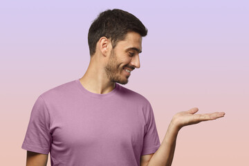 Wall Mural - man isolated on purple background in casual t-shirt demonstrating something on right with palm