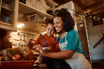 Happy black mother and daughter enjoy in preparing roast turkey for Thanksgiving in kitchen.